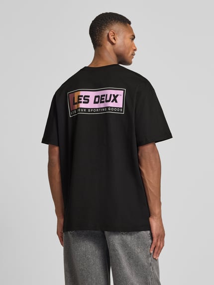 Männermodel trägt T-Shirt mit Logo-Print Modell 'Chase' von Les Deux in Schwarz, Reine Baumwolle, Gerader-Schnitt, Rückenlänge 72 cm, Ganzkörperansicht Rückansicht.