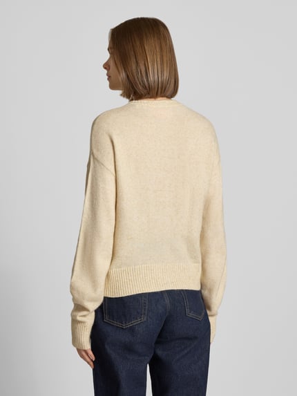 Frauenmodel trägt Cardigan mit Woll-Anteil Modell 'NATALIE' von JJXX in Strick-Optik, beige, Kombination mit blauer Jeans, Ganzkörperansicht Rückansicht.