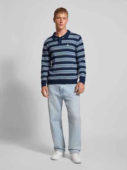 Mężczyzna nosi Sweter z dzianiny 'Strickpullover mit Polokragen in Bouclé-Optik' od REVIEW, krój regular fit, wzór w paski, imitacja bouclé, kołnierzyk polo, listwa guzikowa, wyhaftowane logo, długość tyłu w rozmiarze M 70 cm, długość rękawów 64 cm, jasnoniebieskie odcienie, tekstura miękka, widok całej sylwetki z przodu.