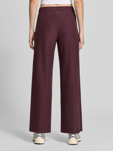 Frauenmodel trägt Wide Fit Sweatpants mit Label-Detail Modell 'CLOUD' von Fabletics in Melange-Bordeaux, elastischer Bund, Ganzkörperansicht Rückansicht. Damen Sweatpants aus elastischem Material-Mix mit Tunnelzug, Innenbeinlänge 75 cm bei Größe S.