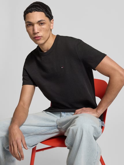 Męskimodel nosi Regular Fit T-Shirt aus reiner Baumwolle od Tommy Jeans, efekt: jednolity kolor, detal z logo, okrągły dekolt, krótki rękaw, dżersej, bawełna. Ujęcie: zbliżenie na górną część ciała