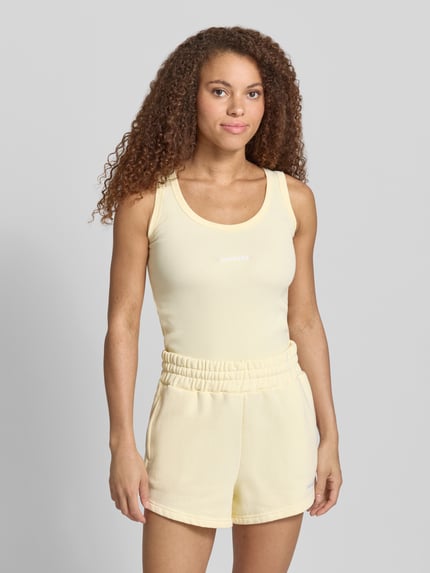 Vrouwenmodel draagt tanktop met logo-stitching model 'CESIS' van Pegador, katoenmix met stretch, fijnrib, ronde hals, nauwsluitend model, ruglengte maat S 52 cm, zachte gele tinten, gladde textuur, geheelvooraanzicht.