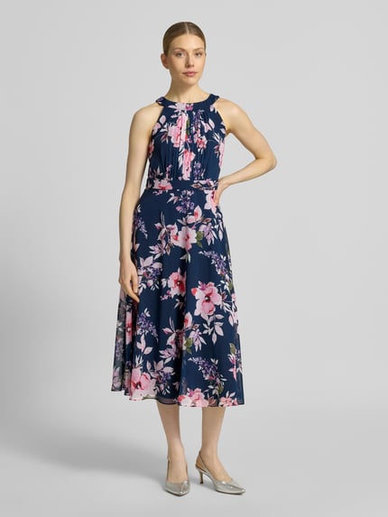 Frauenmodel trägt Midikleid mit floralem Allover-Print von Christian Berg Cocktail in Blau mit Pink-Tönen, Tailliert, Rundhalsausschnitt, Gelegte Falten, Ärmelloses-Design, Nahtreißverschluss, Ganzkörperansicht von vorne. Rückenlänge Größe 36: 115 cm, Brustweite Größe 36: 40 cm.