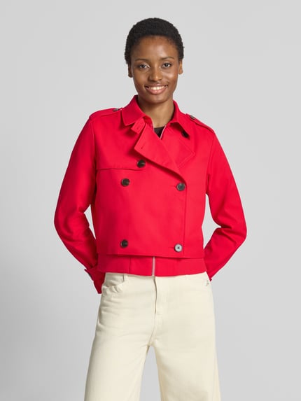 Modelka nosi Kurzer Trenchcoat mit Ärmelriegeln od monari, czerwony, prosty krój, podwójna listwa guzikowa, klapy na ramionach, patki przy mankietach, wykładany kołnierz, zamek błyskawiczny, dodatkowe ściągacze na rękawach, Długość tyłu w rozmiarze 36: 52 cm, Szerokość ramion w rozmiarze 36: 42 cm, Szerokość klatki piersiowej w rozmiarze 36: 55 cm, Długość rękawów w rozmiarze 36: 66 cm, zdjęcie całej sylwetki od przodu
