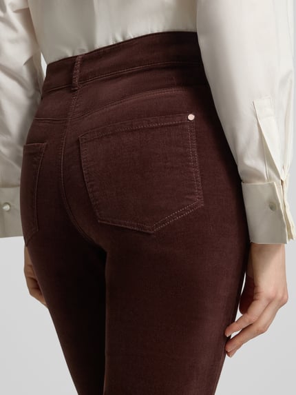 Frauenmodel trägt Slim Fit Stoffhose aus elastischem Baumwoll-Mix von Christian Berg Woman w kolorze ciemnobrązowym, 5 kieszeni, szlufki na pasek, zapięcie na guzik i zamek błyskawiczny, szerokość w rozmiarze 36/32: 38 cm, długość wewnętrzna nogawki: 82 cm, detaliczna faktura materiału, widok z tyłu, detailaufnahme.