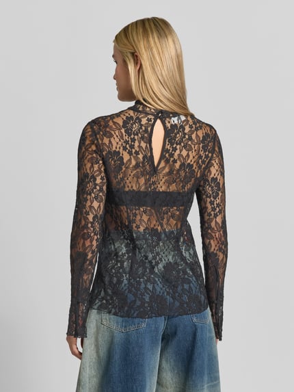 Frauenmodel trägt Langarmbluse aus Spitze Modell 'MEENA' von BAUM & PFERDGARTEN mit floralem Allover-Muster in Schwarz, gerade geschnittener Saum, langarm, blickdichte und transparente Texturen, Ganzkörperansicht Rückansicht.