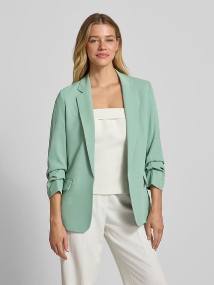 Frauenmodel trägt Regular Fit Blazer mit Reverskragen von Jake*s Collection in Mintgrün, glatte Textur, Pattentaschen, Ganzkörperansicht von vorne. Elastischer Material-Mix, Rückenlänge 69 cm, Brustweite 46 cm, Ärmellänge 52 cm bei Größe 36.