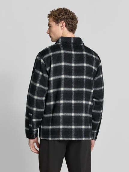 Männermodel trägt Hemdjacke mit Druckknopfleiste von BOSS Orange, kariertes Allover-Muster in Schwarz-Weiß, Ganzkörperansicht Rückansicht.