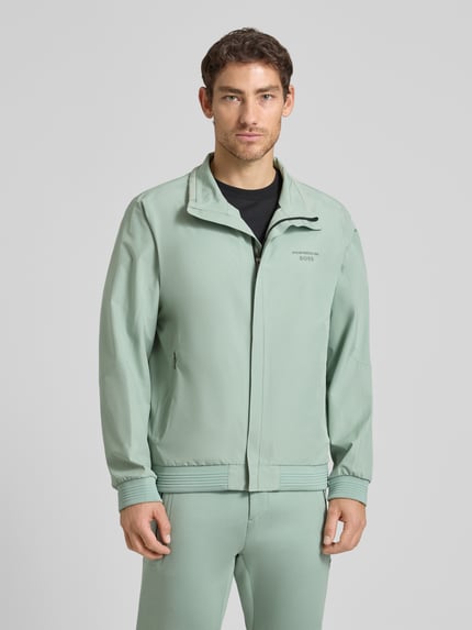 Männermodel trägt Regular Fit Funktionsjacke aus wasserdichtem Material - Porsche x BOSS, Optik: Unifarben, Reißverschlusstaschen, Label-Print, Wärmeisolierung, Stehkragen, Ärmelabschluss und Rumpfabschluss: Gerippt, Ganzkörperansicht von vorne.