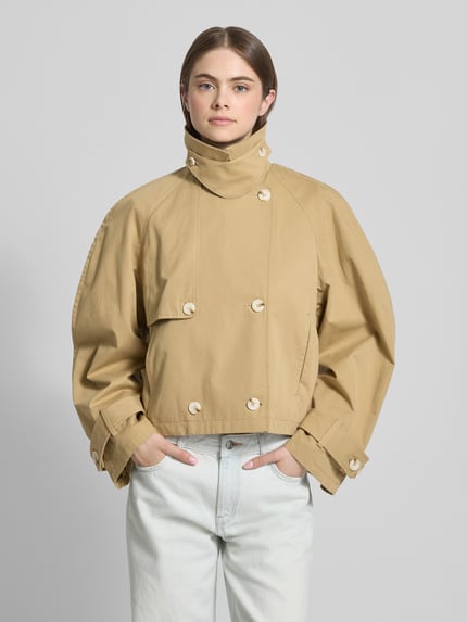 Vrouwenmodel draagt trenchcoat met mouwsluitingen model 'MIA' van Topshop in beige, puur katoen, regular fit, met dubbele rij knopen, platte kraag, knoopsluiting; ruglengte maat S 53 cm, schouderbreedte 52 cm, borstwijdte 54 cm, mouwlengte 64 cm; vooraanzicht bovenlichaam
