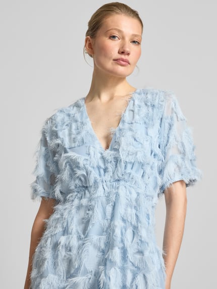 Frauenmodel trägt Cocktailkleid mit Fransen Modell 'PAZYLLA' von YAS in Hellblau, V-Ausschnitt, Midikleid, Nahaufnahme Oberkörper.