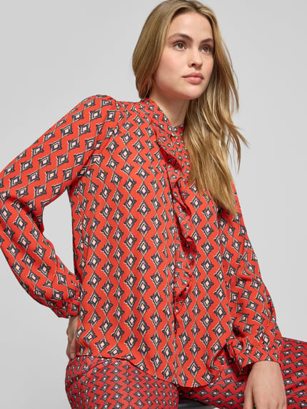 Frauenmodel trägt Regular Fit Bluse im Allover-Look mit Volants von Marc Cain in Rot mit Stehkragen und Schlüsselloch-Ausschnitt, Nahaufnahme Oberkörper.