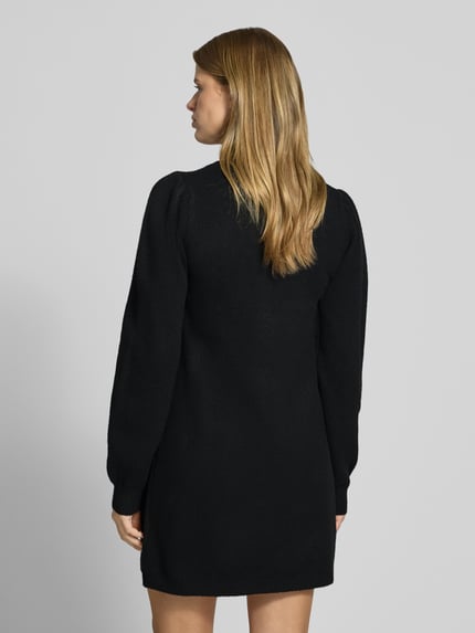 Frauenmodel trägt schwarzes Strickkleid mit Label-Detail von PIECES, glatte Textur, Damen Freizeitkleid, Ganzkörperansicht Rückansicht.