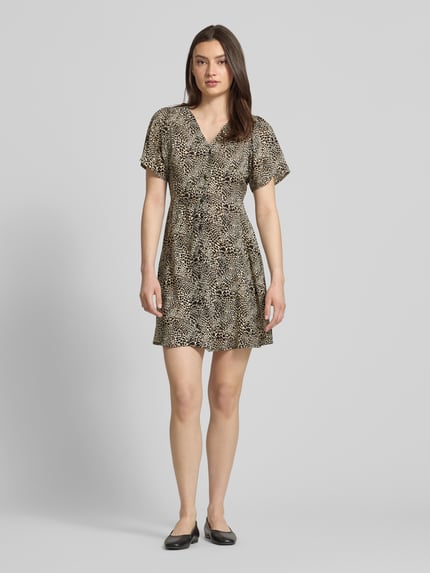 Frauenmodel trägt Minikleid aus reiner Viskose Modell 'EVIDA' von Only mit Allover-Muster, V-Ausschnitt, Taillengürtel, taillierte Passform, Ganzkörperansicht von vorne.