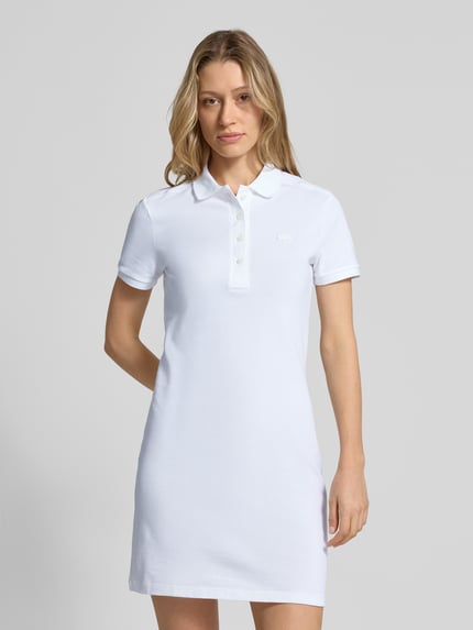 Frauenmodel trägt Slim Fit Polokleid aus Baumwoll-Mix von Lacoste in Weiß mit kurzer Knopfleiste, Logo-Stitching, Ganzkörperansicht von vorne.