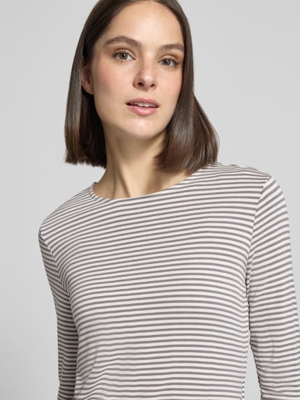 Kobiece model prezentuje bluzkę z długim rękawem z mieszanki wiskozy o kroju slim fit, z okrągłym dekoltem, model 'Kamaja' od someday, długość tyłu w rozmiarze 36: 57 cm, paski, jasne kolory. Zbliżenie górnej części ciała.