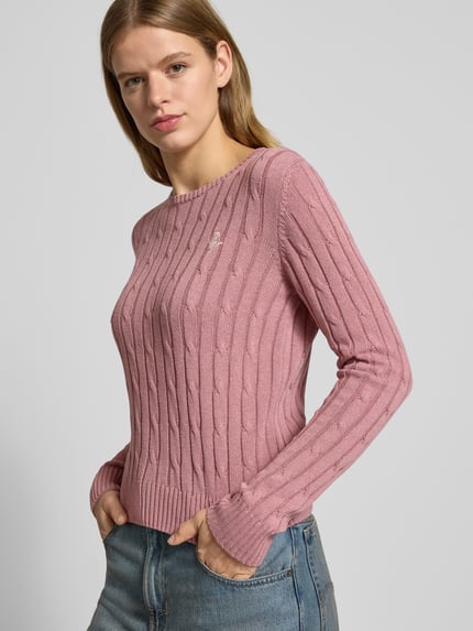 Frauenmodel trägt Slim Fit Strickpullover mit Rundhalsausschnitt und Zopfmuster von Review aus Baumwoll-Mix in Rosa mit Label-Stitching, Nahaufnahme Oberkörper.