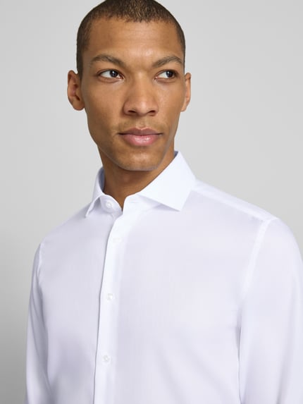 Mannelijk model draagt Slim Fit Business-Hemd aus Baumwolle met Kentkraag van SEIDENSTICKER, wit, fijn gestructureerd, knoopsluiting, detailopname bovenlichaam.