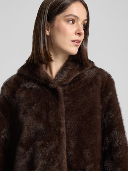 Młody modelka nosi Mantel mit Kapuze und Eingrifftaschen od Rinascimento, ciemnobrązowy, sztuczne futro, krój prosty, kaptur, kieszenie boczne, długość pleców w rozmiarze S: 101 cm, zbliżenie na górną część ciała.