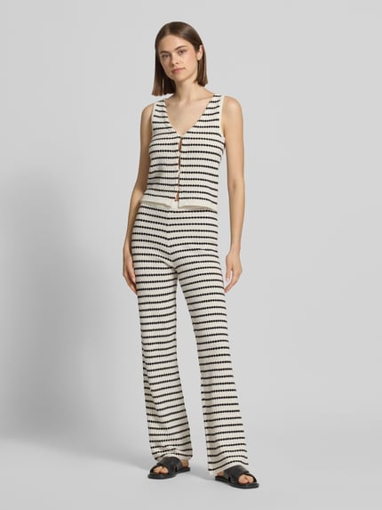 Frauenmodel trägt Strickweste mit V-Ausschnitt und Knopfleiste von REVIEW im Allover-Look, Material-Mix mit Baumwoll-Anteil, Regular-Fit, creme und schwarz, Ganzkörperansicht von vorne.