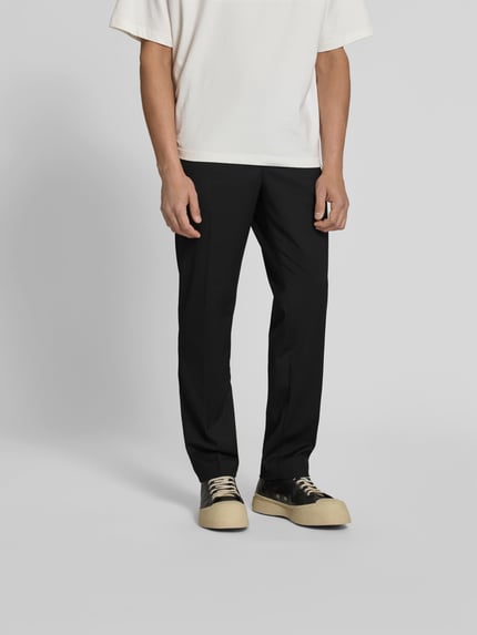 Mężczyzna nosi Slim Fit Anzughose mit Woll-Anteil od Filippa K, elastyczna mieszanka materiałów z dodatkiem wełny, krój slim fit, zapięcie na guzik i zamek błyskawiczny, wpuszczane kieszenie z przodu i kieszenie z tyłu, zakładki w pasie, długość wewnętrzna nogawki w rozmiarze 50: 80 cm, szerokość w rozmiarze 50: 36 cm, czarny kolor, prosta forma, matowa tekstura, całkowity widok z przodu