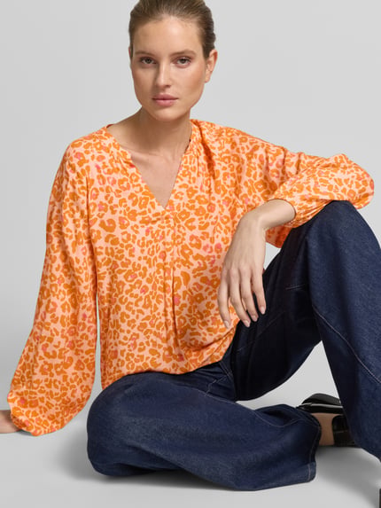 Frauenmodel trägt Damenbluse im Allover-Look mit V-Ausschnitt von Emily Van den Bergh in Orange-Rosa, reine Viskose, Nahaufnahme Oberkörper.