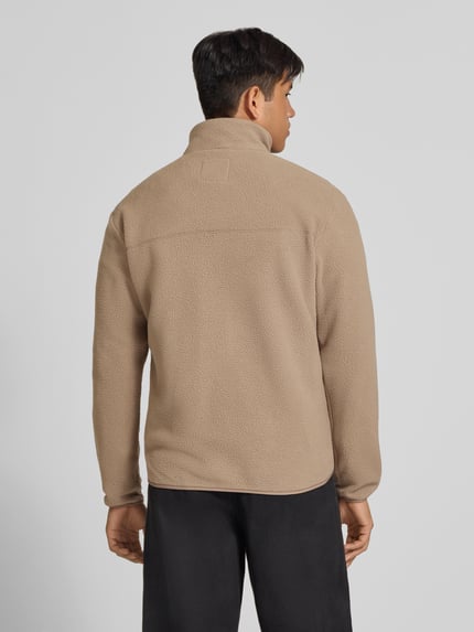 Męski model nosi kurtkę z polaru o kroju regular fit ze stójką, model 'JASON' od ONLY, beżowy kolor, tekstura miękka, widok całej sylwetki od tyłu.