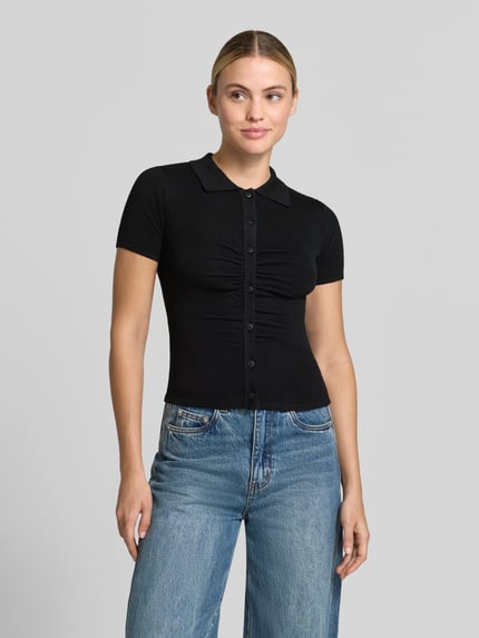 Frauenmodel trägt Slim Fit Cardigan mit Woll-Anteil von MANGO, schwarz, kurzärmelig, Knopfleiste, Umlegekragen, glatte Textur, Ganzkörperansicht von vorne.