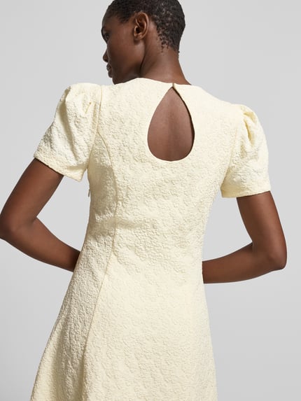Vrouwenmodel draagt Midikleid met floralem Allover-Detail van ROTATE, elastische materiaalmix, getailleerd, A-lijn, korte mouw, detailopname rugaanzicht.