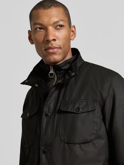 Männermodel trägt Funktionsjacke mit gewachstem Twill von Barbour in Schwarz, glatte Textur, Stehkragen, Nahaufnahme Oberkörper
