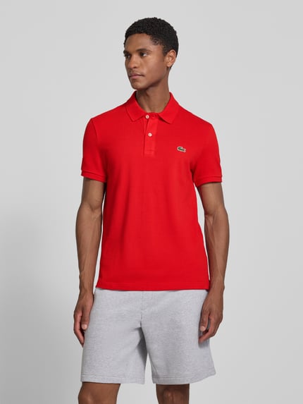 Męski model nosi Slim Fit Poloshirt aus reiner Baumwolle von Lacoste, kolor czerwony, jednolita faktura, Ganzkörperansicht von vorne.