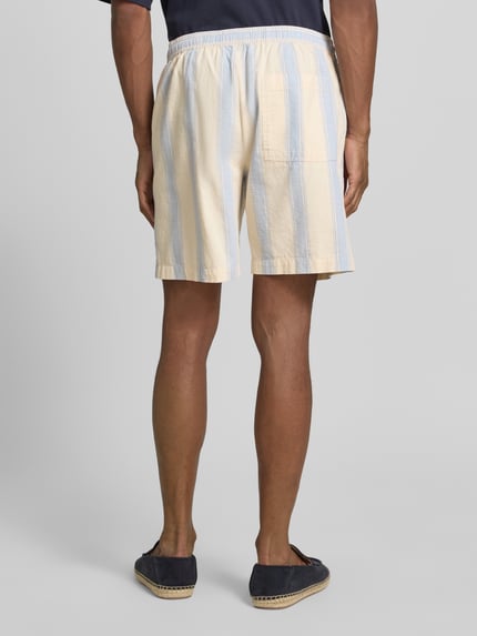 Männermodel trägt Regular Fit Shorts aus reiner Baumwolle von Armedangels mit Optik:Allover-Muster, Gestreift, Twill, Ganzkörperansicht Rückansicht.