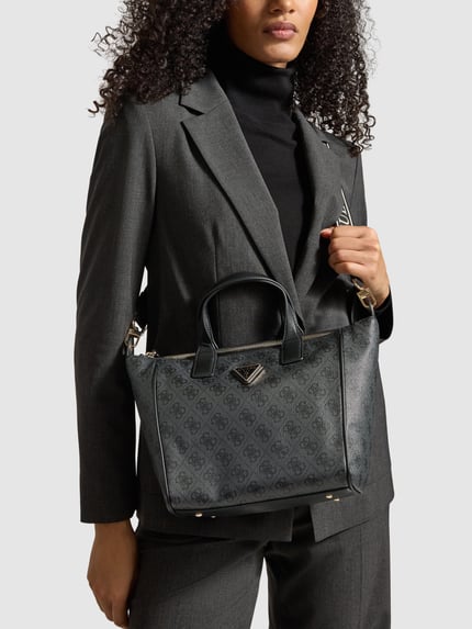 Vrouwenmodel draagt Tote Bag met Labeldetail model 'FOLLIE' van Guess in zwartgrijs met draagbanden en afneembare schouderband, hoofvak met ritssluiting, binnenvak met ritssluiting, breedte 35 cm, lengte 23 cm, diepte 11 cm, bandlengte 104 cm, gladde textuur, geometrisch patroon, kleurenmix donkergrijs en zwart. Nahaufnahme Oberkörper.
