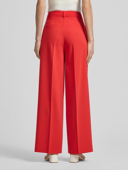 Frauenmodel trägt rote Hose mit Bügelfalten von More & More, Material-Mix mit Viskose-Anteil, Regular-Fit, Gesäßtaschen, Ganzkörperansicht Rückansicht.