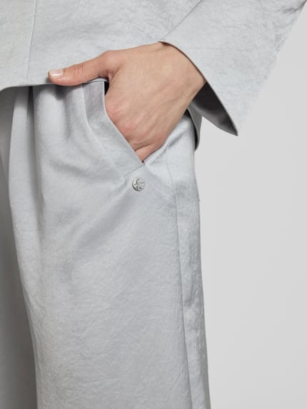 Frauenmodel trägt Wide Fit Stoffhose mit gelegten Falten von Marc Cain aus Acetat-Mix mit Eingrifftaschen, Nahaufnahme Oberkörper.