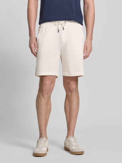 Männermodel trägt Regular Fit Shorts mit Tunnelzug Modell 'JUANITO' von JOOP! Collection aus Reiner Baumwolle in Beige, Ganzkörperansicht von vorne.