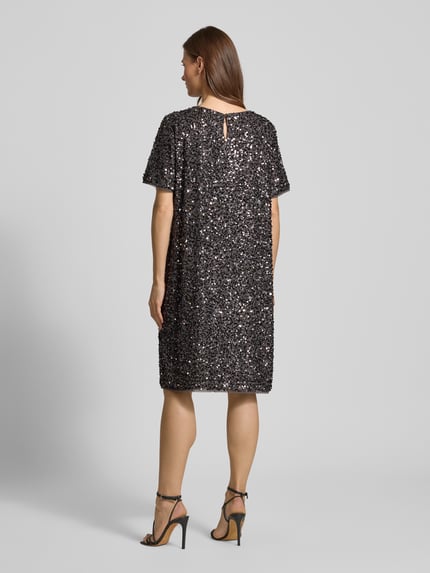 Vrouwenmodel draagt Knielanges Kleid mit Rundhalsausschnitt van Comma, los model, knielengte, met pailletten, ronde hals, met korte mouwen, ruglengte maat 36: 96 cm, borstwijdte maat 36: 53 cm, mouwlengte maat 36: 25 cm, kleurenmix van zwart en zilver, glanzende textuur, recht model, Ganzkörperansicht Rückansicht.