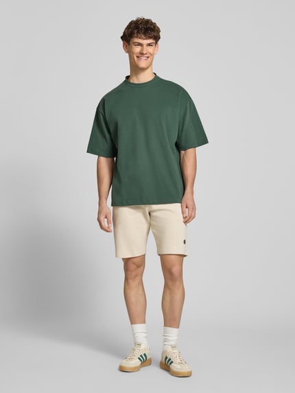 Männermodel trägt Straight Fit Shorts mit Logo-Stitching Modell 'Fillip' von Blend aus Reine Baumwolle mit Strukturmuster, Eingrifftaschen, Gesäßtaschen sowie elastischem Bund mit Tunnelzug, Ganzkörperansicht von vorne.