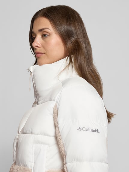 Frauenmodel trägt Steppjacke mit Stehkragen Modell 'Leadbetter Point II' von Columbia in Weiß mit sichtbarem Reißverschluss, Nahaufnahme Oberkörper. Damen Steppjacke, Regular Fit, Eingrifftaschen, strukturierte Oberfläche, Kontext: Rückenlänge 60 cm, Schulterbreite 41 cm, Brustweite 52 cm, Ärmellänge 61 cm.