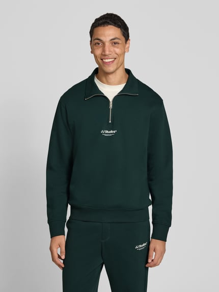 Männermodel trägt Regular Fit Sweatshirt aus Baumwoll-Mix Modell 'Soho' von JACK & JONES in Dunkelgrün mit Logo-Print, Ganzkörperansicht von vorne.