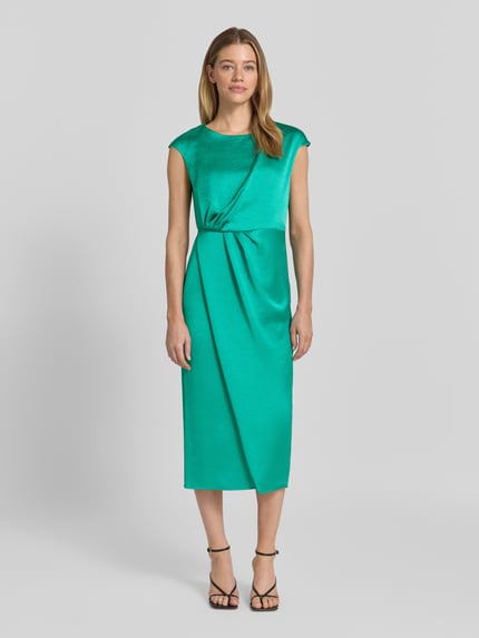 Modelka kobieca nosi sukienka midi z satyny z drapowaniami Midikleid aus Satin mit Drapierungen von Marc Cain, prosty krój, okrągły dekolt, zamek błyskawiczny z tyłu, długość tyłu w rozmiarze 36: 115 cm, szerokość w rozmiarze 36: 37 cm, kolor zielony, gładka tekstura, widok całej sylwetki z przodu.