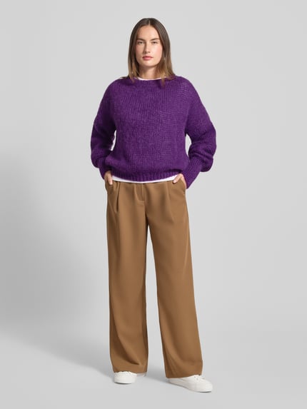 Frauenmodel trägt Oversized Strickpullover mit Rundhalsausschnitt Modell 'Isolde' von LOLLYS LAUNDRY aus Material-Mix mit Mohair-Anteil, lila Farbe, gerippte Abschlüsse, zu weiter brauner Hose und weißen Sneakers, Ganzkörperansicht von vorne.
