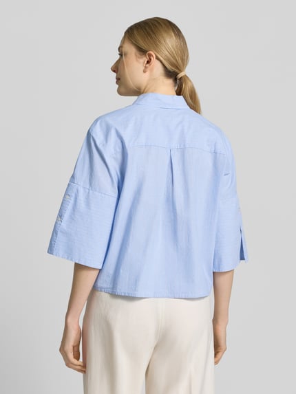 Frauenmodel trägt Boxy Fit Bluse aus Baumwolle mit Knopfleiste von Emily Van den Bergh in Hellblau, Reine Baumwolle, Hemdblusenkragen, Rückenlänge bei Größe 36: 54 cm, Ärmellänge in 3/4-Ärmellänge, Boxy-Fit, Ganzkörperansicht Rückansicht.