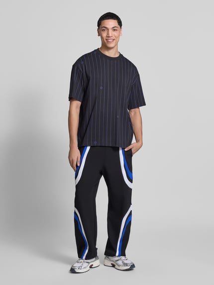 Mannelijk model draagt Relaxed Fit Sweatpants aus Baumwoll-Mix model 'Nalotron' van Hugo Blue met effen kleuren, contraststrepen, elastische boord, tunnelkoord aan de pijpen, zij-steekzakken, materiaalverwerking sweat, katoenmix, kleuren zwart met blauwe en witte accenten, volledige lichaamsvooraanzicht.