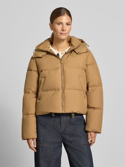 Frauenmodel trägt Pufferjacke mit Kapuze von LACOSTE, unifarben, cropped, Logo-Stitching, Kapuze, Reißverschluss, seitliche Taschen, Ganzkörperansicht von vorne.