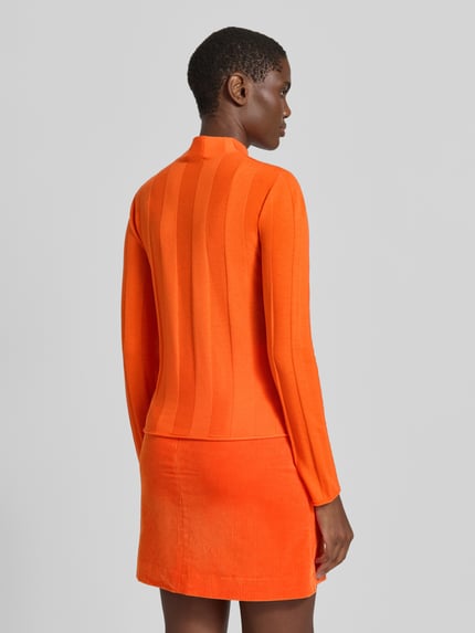 Frauenmodel trägt Strickpullover aus Schurwolle-Mix mit Stehkragen von Marc Cain in Orange, Slim Fit, Rückenlänge 55 cm, Ganzkörperansicht Rückansicht.