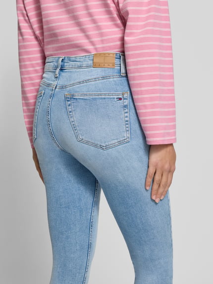 Kobieta nosi Skinny Fit Jeans aus Baumwoll-Mix Modell 'NORA' od Tommy Jeans, jasnoniebieski denim, Ganzkörperansicht Rückansicht, damskie jeansy skinny fit od Tommy Jeans
