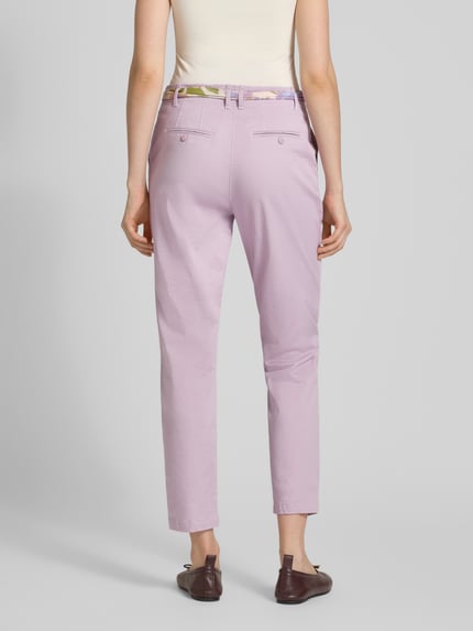 Kobiece modelka nosi Slim Fit Chino mit Viskose-Anteil od Christian Berg Woman w kolorze jasnofioletowym, elastyczna bawełna z wiskozą, krój slim fit, skrócona długość, zdejmowany materiałowy pasek, zapięcie na guzik i zamek, widok całej sylwetki z tyłu.