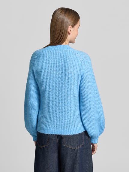 Frauenmodel trägt Pullover mit Ballonärmeln Modell 'Siforo' von HUGO in Hellblau, Strickoptik, Strukturmuster, Ganzkörperansicht Rückansicht.