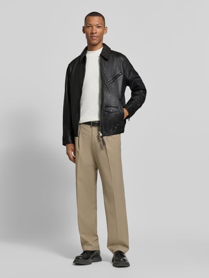Męski model nosi Regular Fit Lederjacke aus Schafsleder od AllSaints, czarna skóra owcza, zamek błyskawiczny dwustronny, kieszeń na piersi, kieszenie boczne i z patką, Model 'arto', kołnierzyk typu kent, widok całej sylwetki z przodu.